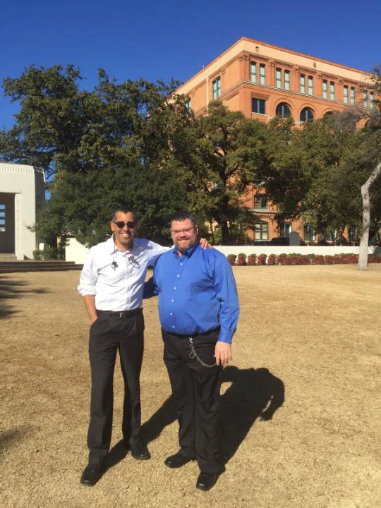 Phillip Babich standing in front of the Book Depository in Dallaswith a U.S. Army Veteran client following a successful pro bono appeal before the Board of Veterans Appeals.